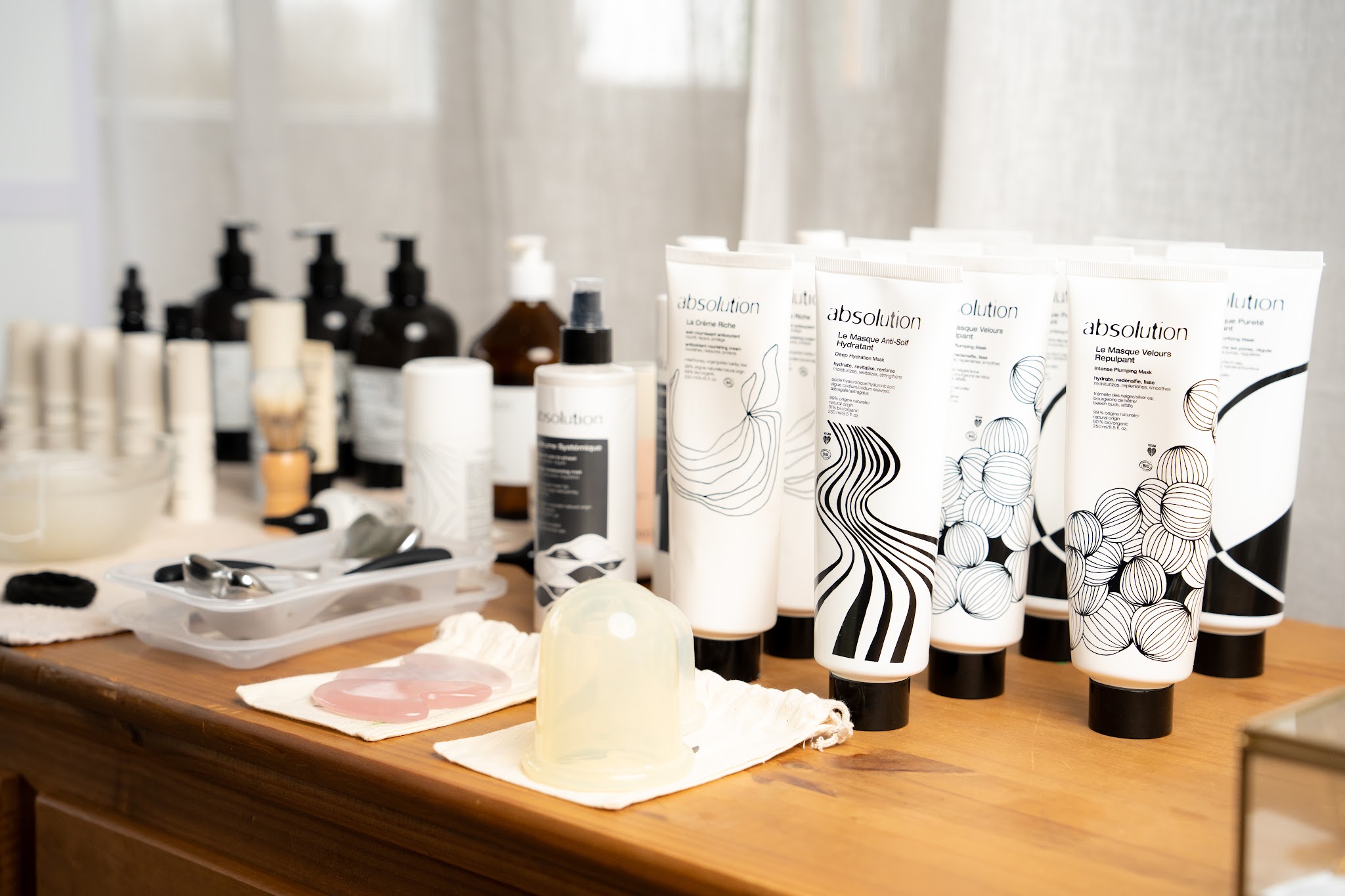 Absolution tubes en flesjes met een gua sha steen op een houten tafel in de salon
